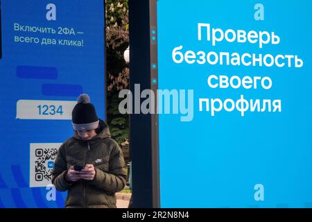 Moskau, Russland. 20. Mai 2023. Ein junger Mann überprüft Ihr Telefon in der Nähe des VKontakte Social Network Ständer mit Sicherheitsinformationen für die Benutzer sozialer Netzwerke im Gorky Park in Moskau, Russland. Der Stand spricht über die Möglichkeit, zwei-Faktor-Identifikation für Autorisierungsbenutzer auf dem Vkontakte-Portal zu verbinden. Auf dem rechten Banner steht „Überprüfen Sie die Sicherheit Ihres Profils“. Stockfoto