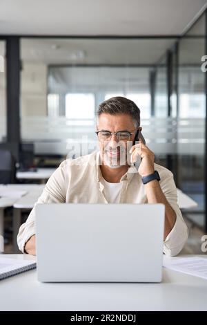 Vertikales Porträt eines erwachsenen Hispanikers, der am Arbeitsplatz per Mobiltelefon spricht Stockfoto