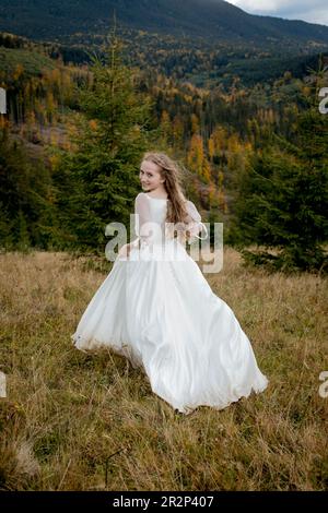 Die Braut rennt den Hügel hinunter und hebt das herrliche Kleid. Stockfoto