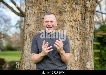 Ein grauhaariger Mann stand verzweifelt vor einem Baum im Park Stockfoto