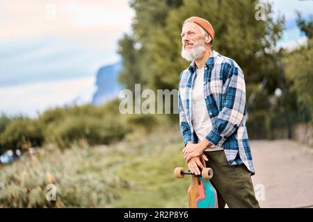 Ein älterer Hipster-Skater steht im Naturpark und hält Schlittschuh. Stockfoto