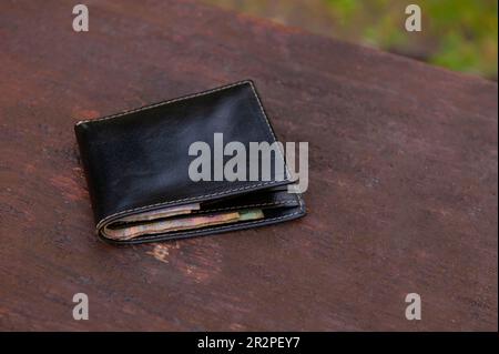 Schwarze Geldbörse auf Holzbank im Freien. Verloren und gefunden Stockfoto