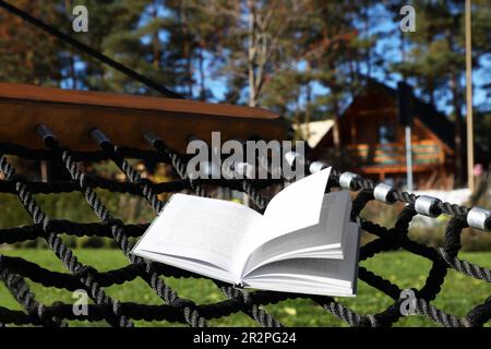 Komfortable NetzHängematte mit offenem Buch im Freien an sonnigen Tagen Stockfoto