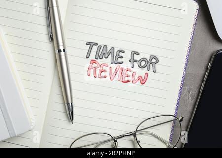 Notizblock mit Text Time for Review, Stift, Brille und Mobiltelefon auf grauem Tisch, flach liegend