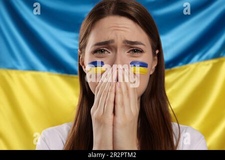 Traurige junge Frau mit gefalteten Händen nahe der ukrainischen Flagge Stockfoto