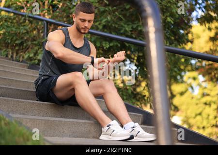 Attraktiver, seriöser Mann, der nach dem Treppentraining im Park den Puls überprüft Stockfoto