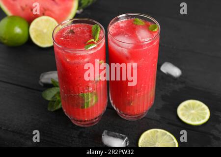 Gläser köstlicher frischer Wassermelonensaft, Limette, Minze und Eis auf einem schwarzen Holztisch Stockfoto