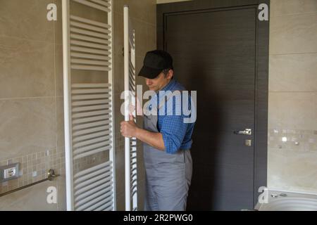 Bild eines Klempners, während er einen Heizkörper wie einen Handtuchwärmer in einem Badezimmer zu Hause zusammenbaut. Stockfoto