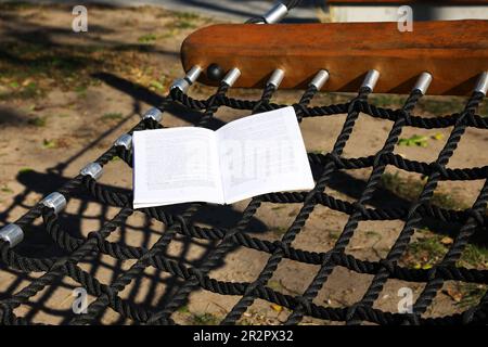 Komfortable NetzHängematte mit offenem Buch im Freien an sonnigen Tagen Stockfoto