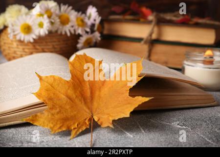 Offenes Buch, Herbstblatt und Duftkerze auf hellgrauem, strukturiertem Tisch, Nahaufnahme Stockfoto