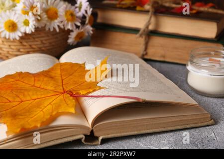 Buch mit Herbstblatt als Lesezeichen und Duftkerze auf hellgrauem, strukturiertem Tisch, Nahaufnahme Stockfoto