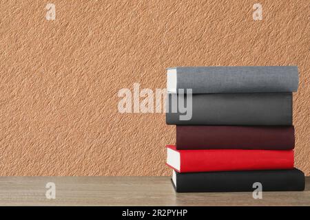 Viele gestapelte Bücher mit festem Einband auf einem Holztisch vor beigefarbenem strukturiertem Hintergrund, Platz für Text Stockfoto