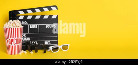 Köstliches Popcorn, Gläser, Klebeband und Klappbrett auf gelbem Hintergrund, Platz für Text. Bannerdesign Stockfoto