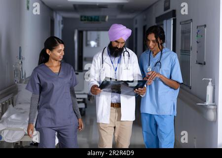 Verschiedene männliche und weibliche Ärzte, die Röntgenaufnahmen machen und die Arbeit im Korridor des Krankenhauses diskutieren Stockfoto