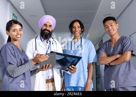 Portrait von glücklichen, vielfältigen Ärzten und Ärztinnen, die Röntgen und Tablette im Korridor des Krankenhauses halten Stockfoto