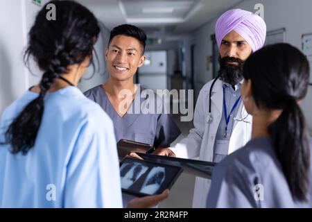 Verschiedene männliche und weibliche Ärzte halten Röntgen und Tablette, sprechen im Flur im Krankenhaus Stockfoto