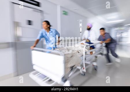 Diverse Ärzte drängen Patienten im Bett im Flur des Krankenhauses Stockfoto