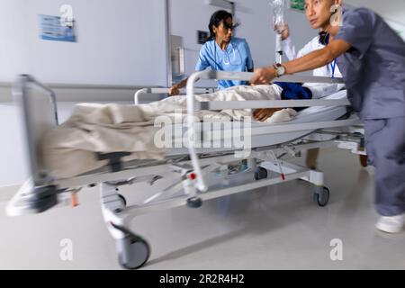 Diverse Ärzte drängen Patienten im Bett im Flur des Krankenhauses Stockfoto