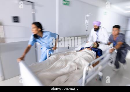 Diverse Ärzte drängen Patienten im Bett im Flur des Krankenhauses Stockfoto