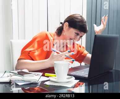 Porträt einer glücklichen Geschäftsfrau am Arbeitsplatz im Büro. Schöne junge Frau, die mit einem modernen Laptop lächelt und lächelt und eine Videokonferenz veranstaltet. Stockfoto
