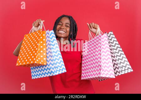 Afrikanische Frau, die viele Einkaufstaschen hebt, während sie vor der Kamera lächelt Stockfoto