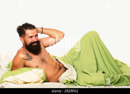 Der junge Mann liegt auf dem Bett und genießt den Morgen. Attraktiver bärtiger Kerl, der in den Händen das Kissen im Bett hält. Der Junge schläft und träumt Stockfoto