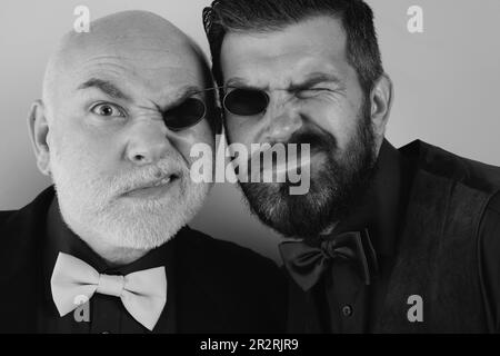 Vater und bärtiger Sohn täuschen sich herum. Gläser für zwei Personen. Herren in Anzügen und Fliege. Seelenverwandte. Familienbetrieb. Familientraditionen. Isoliert auf einem Stockfoto