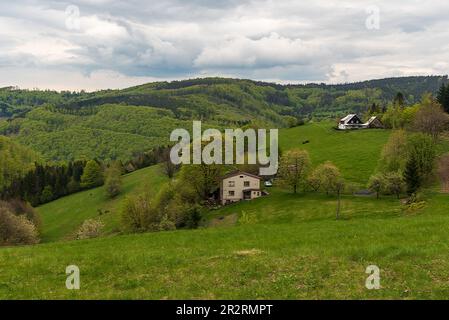 Frühling auf Filipka im Slezske Beskydy-Gebirge in der tschechischen republik mit Wiese mit Bäumen und einigen Gebäuden und waldbedeckten Hügeln auf der Rückseite Stockfoto