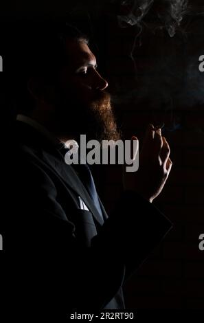 Mann, der Zigarette raucht, isoliert auf Schwarz. Ein Mann raucht Cannabis-Unkraut, ein Gelenk und ein Feuerzeug in seinen Händen. Rauch auf schwarzem Hintergrund. Konzepte von Stockfoto