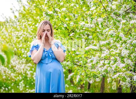 Eine schwangere Frau im Garten blühender Apfelbäume ist allergisch. Selektiver Fokus. Die Natur. Stockfoto