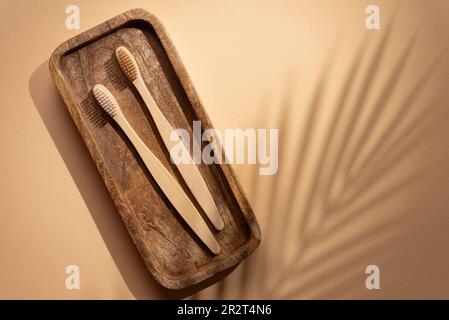 Umweltfreundliche Bambuszahnbürsten mit Palmenblattschatten auf gelbem Hintergrund. Natürliches Bio-Kosmetikprodukt-Konzept für Badezimmer. Stockfoto