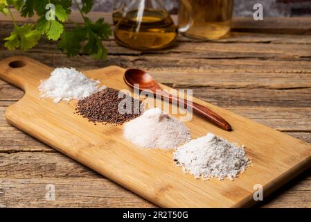 Holzbrett mit verschiedenen Salzstapeln, schwarz, rosa, flachgelegt und mit Trüffeln gewürzt, auf rustikalem Holzhintergrund. Stockfoto