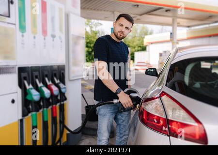 Ein hübscher Mann betankt sein Auto an einer Selbstbedienungs-Tankstelle. Männlich, der Dieselkraftstoff im Auto mit einer Zapfpistole betankt. Benzinkonzept. Stockfoto