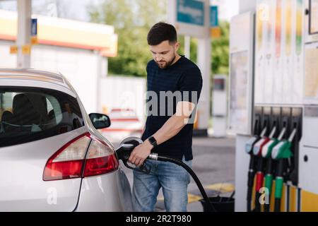 Ein hübscher junger Mann betankt an der Tankstelle ein Auto. Männlich, der Dieselkraftstoff im Auto mit einer Zapfpistole betankt. Benzinkonzept. Seitenansicht Stockfoto