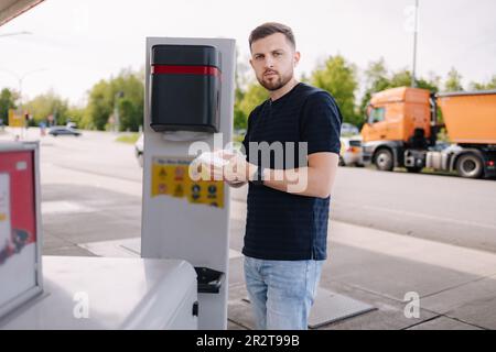 Der junge Mann wischt sich die Hände mit einer nassen Serviette, nachdem er das Auto an der Tankstelle betankt hat Stockfoto