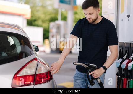 Ein gutaussehender bärtiger Mann betankt das Auto an der Selbstbedienungs-Tankstelle. Benzinkonzept Stockfoto