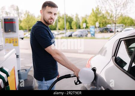 Ein hübscher Mann betankt sein Auto an einer Selbstbedienungs-Tankstelle. Männlich, der Dieselkraftstoff im Auto mit einer Zapfpistole betankt. Benzinkonzept. Stockfoto