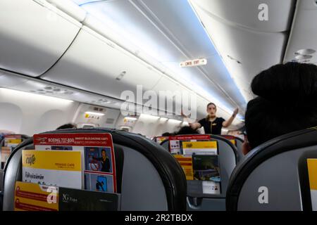 Weibliche Flugbegleiterin aus dem Fokus zeigt Fluggästen, die auf Stühlen sitzen, Notausgänge in einer Boeing 737-800, Pegasus Airline, türkische Fluggesellschaft Stockfoto