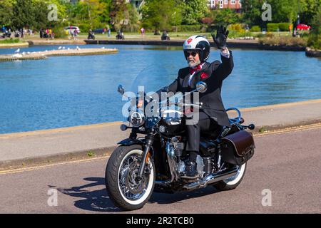 Poole, Dorset, Großbritannien. 21. Mai 2023 Bournemouth and Poole Distinguished Gentlemen’s Ride ist eine von vielen weltweit jährlich stattfindende Veranstaltung, um Geld und Bewusstsein für die Gesundheit von Männern zu schaffen. Im Rahmen der Fahrt fahren Hunderte von Motorrädern, viele davon im Vintage-Stil, durch den Poole Park auf dem Weg nach Bournemouth mit vielen ihrer Fahrer, die angemessen gekleidet sind, in Krawatten im Retro-Stil, Schnurrbart und Tweeds an einem schönen sonnigen Tag. Älterer alter Mann gekleidet in Anzug Jacke und Fliege fahren Triumph Bonneville Speedmaster Motorrad Waving Credit: Carolyn Jenkins/Alamy Live News Stockfoto