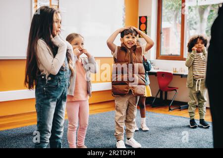 Die Kinder singen und ziehen in der Klasse zu einem Lehrreim über. Gruppe von Grundschulkindern, die an einer Klassenaktivität mit Unterricht von teilnehmen Stockfoto