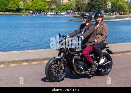 Poole, Dorset, Großbritannien. 21. Mai 2023 Bournemouth and Poole Distinguished Gentlemen’s Ride ist eine von vielen weltweit jährlich stattfindende Veranstaltung, um Geld und Bewusstsein für die Gesundheit von Männern zu schaffen. Im Rahmen der Fahrt fahren Hunderte von Motorrädern, viele davon im Vintage-Stil, durch den Poole Park auf dem Weg nach Bournemouth mit vielen ihrer Fahrer, die angemessen gekleidet sind, in Krawatten im Retro-Stil, Schnurrbart und Tweeds an einem schönen sonnigen Tag. Mann mit weiblichem Sozius, beide in Jacken und Krawattenfahren Triumph Triumph Speed Twin Motorrad Credit: Carolyn Jenkins/Alamy Live News Stockfoto