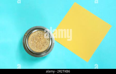Südindische hausgemachte Filterkaffeetasse und gelbes Papier auf blauem Hintergrund. Stockfoto