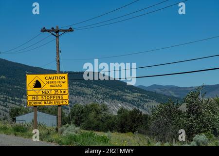 Ansicht eines gelben Warnschilds entlang der Straße in der bergigen Gegend von Kamloops, BC, Kanada, Anzeige der Gefahr des Fließens von Trümmern für die nächsten 35 km bei Regen Stockfoto