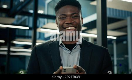Afrikanischer Geschäftsmann junger männlicher Unternehmer Benutzer Executive Worker Angestellter ethnischer Mann Textnachricht am Telefon lächelnd lesen gute mobile Benachrichtigung Stockfoto