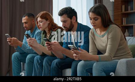 Trauriger Mann, schau dir Freunde an, Handy-süchtig, multiethnische Menschen, die sich in Gadgets verirrt haben, übermäßig nutzen soziale Netzwerke, um online zu chatten, verschiedene langweilige Frauen Stockfoto