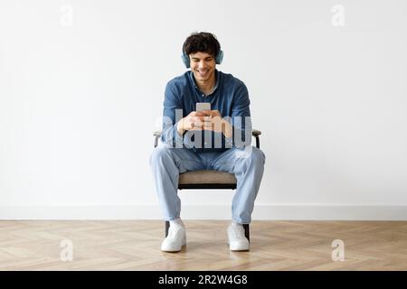 Ein Araber im Sessel, der zu Hause ein Headset mit einem Smartphone trägt Stockfoto
