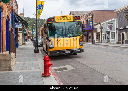 Ein gelber amerikanischer Schulbus, der vor einem roten Feuerhydranten und vor der Kulisse von Park City im Summit County, Utah, USA, geparkt ist Stockfoto