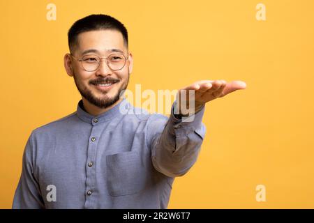 Lächelnder junger asiatischer Mann, der sich die Hand ausstreckt, und etwas Unsichtbares auf seiner Hand hält Stockfoto