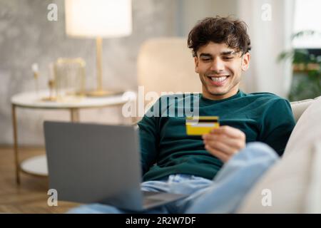Ein Kerl, Der Im Innenbereich Mit Laptop Und Kreditkarte Online Einkauft Stockfoto