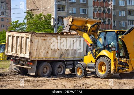 Eine große Traktorschaufel gießt Erde auf einer Straßenbaustelle in das Heck eines großen Lkws. Stockfoto